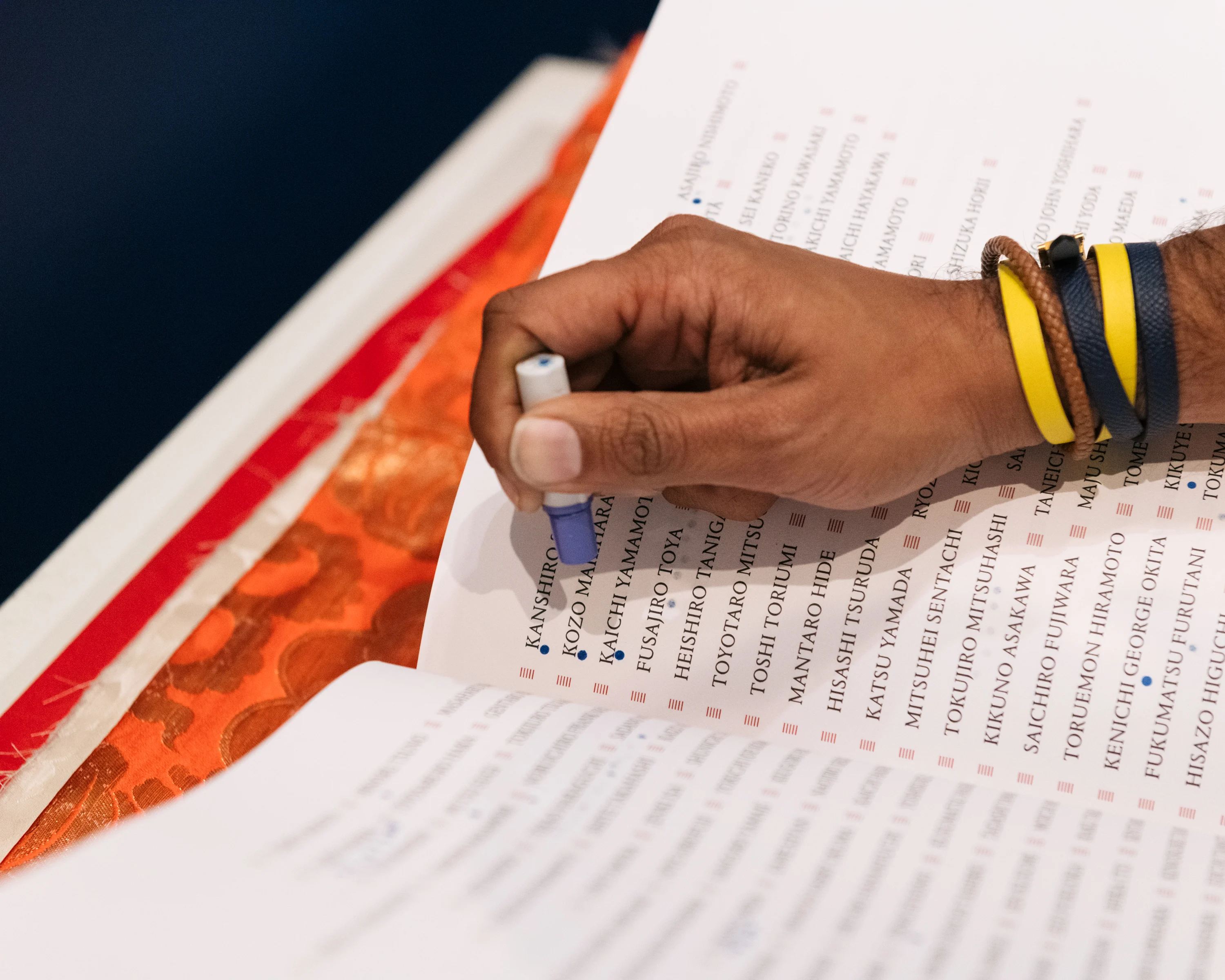 A hand with several rubber bracelets on the wrist makes notations on a page in a book.