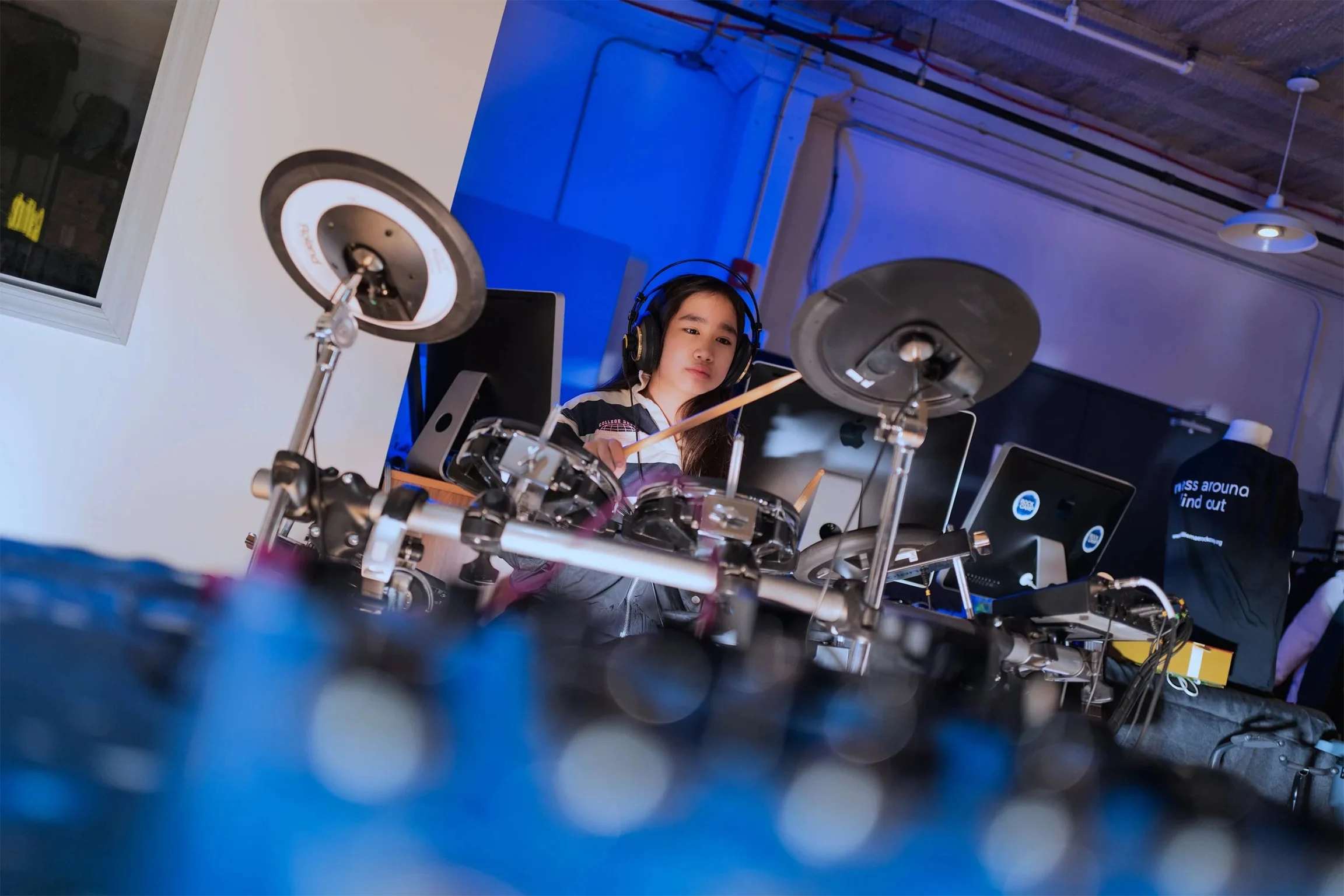 A young music student is wearing headphones and playing the drums.