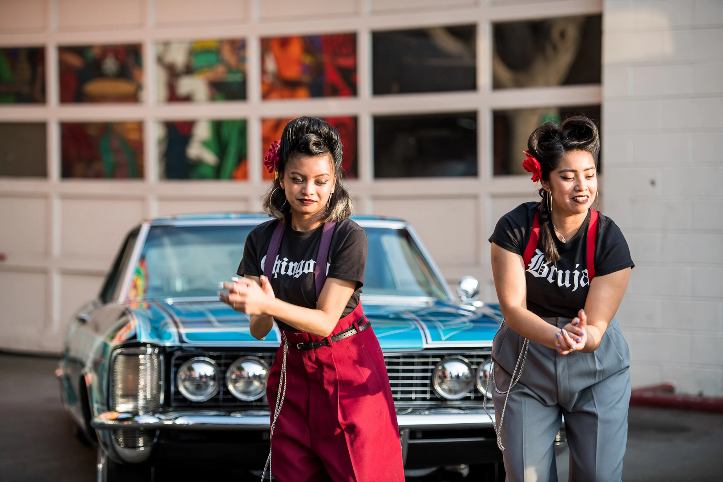 Two dancers wearing streetwear stand before a vintage car and clap their hands