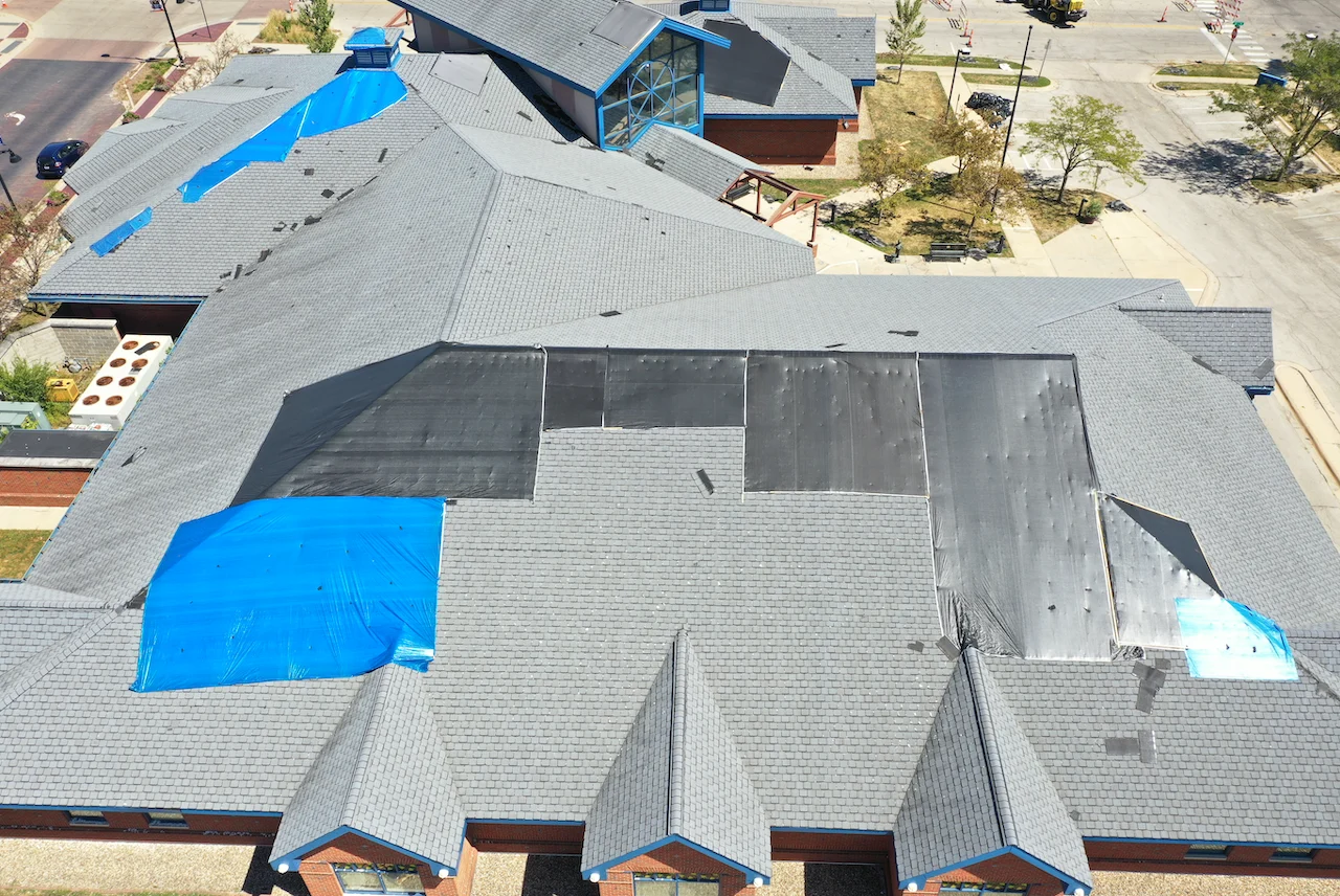An aerial view of a building shows its roof is patched with tarps of different sized.