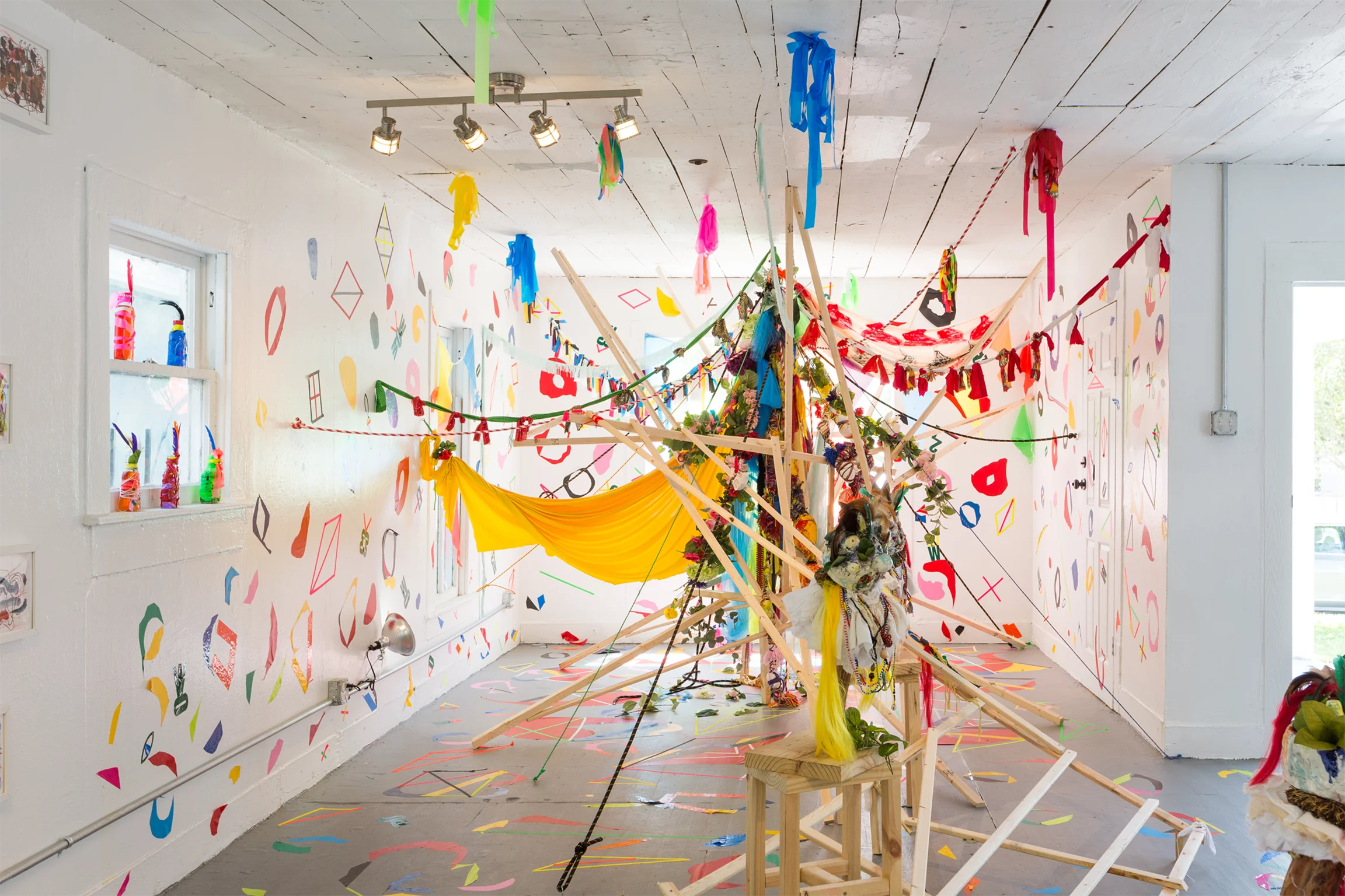 A white walled and ceilinged room with multicolored streamings hanging from the walls and ceiling forming a web in the middle