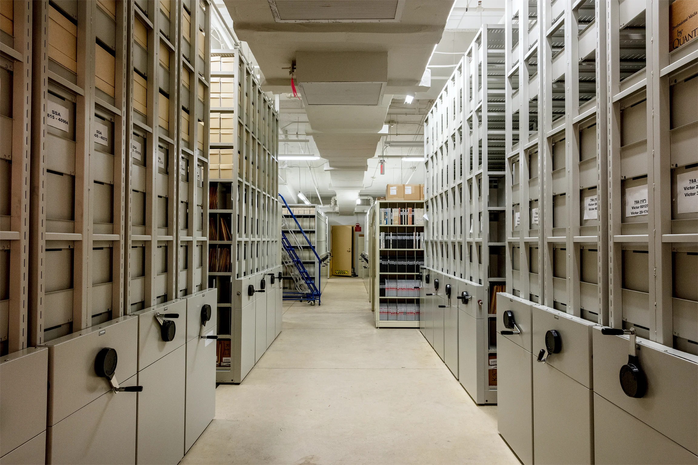 A view down a long basement hallway lit by fluorescent lights with tall gray filing cabinets on both sides