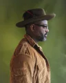 A side profile of a Black poet who is wearing glasses and a hat with a feather hat pin.
