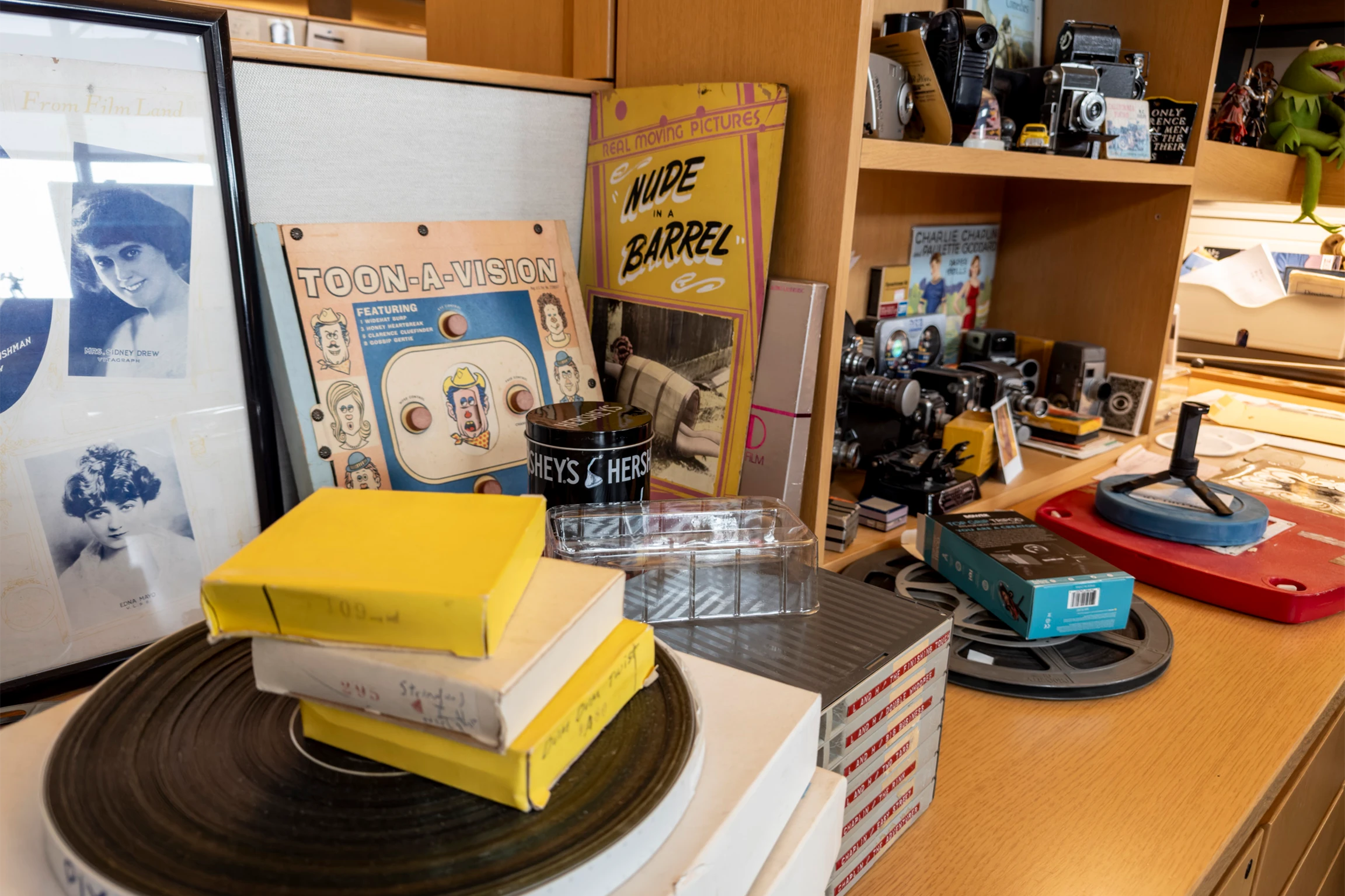 A brown wooden desk and bookshelf containing various items such as books, records, and vintage posters