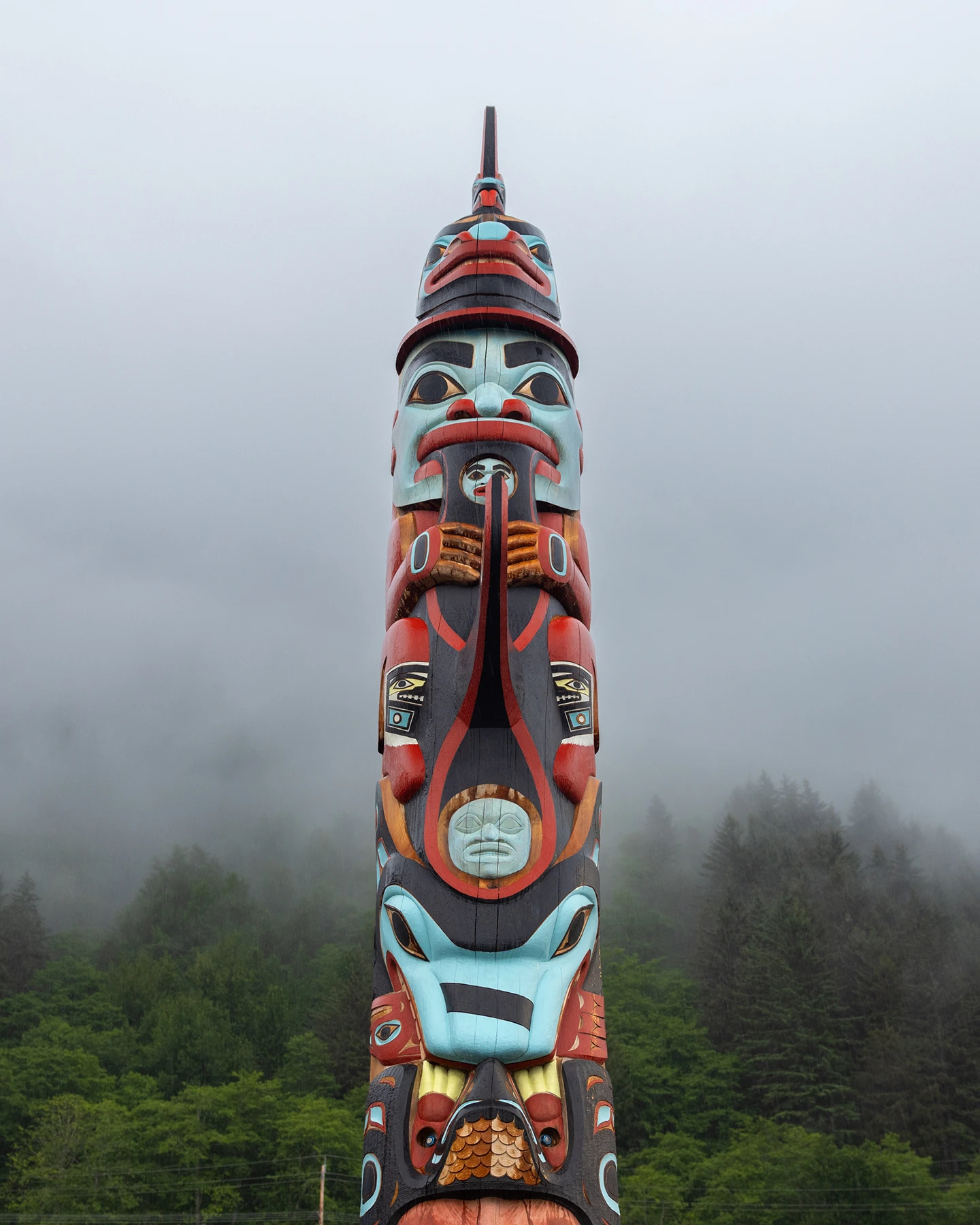 A multicolored painted totem pole set in front of a foggy forest landscape