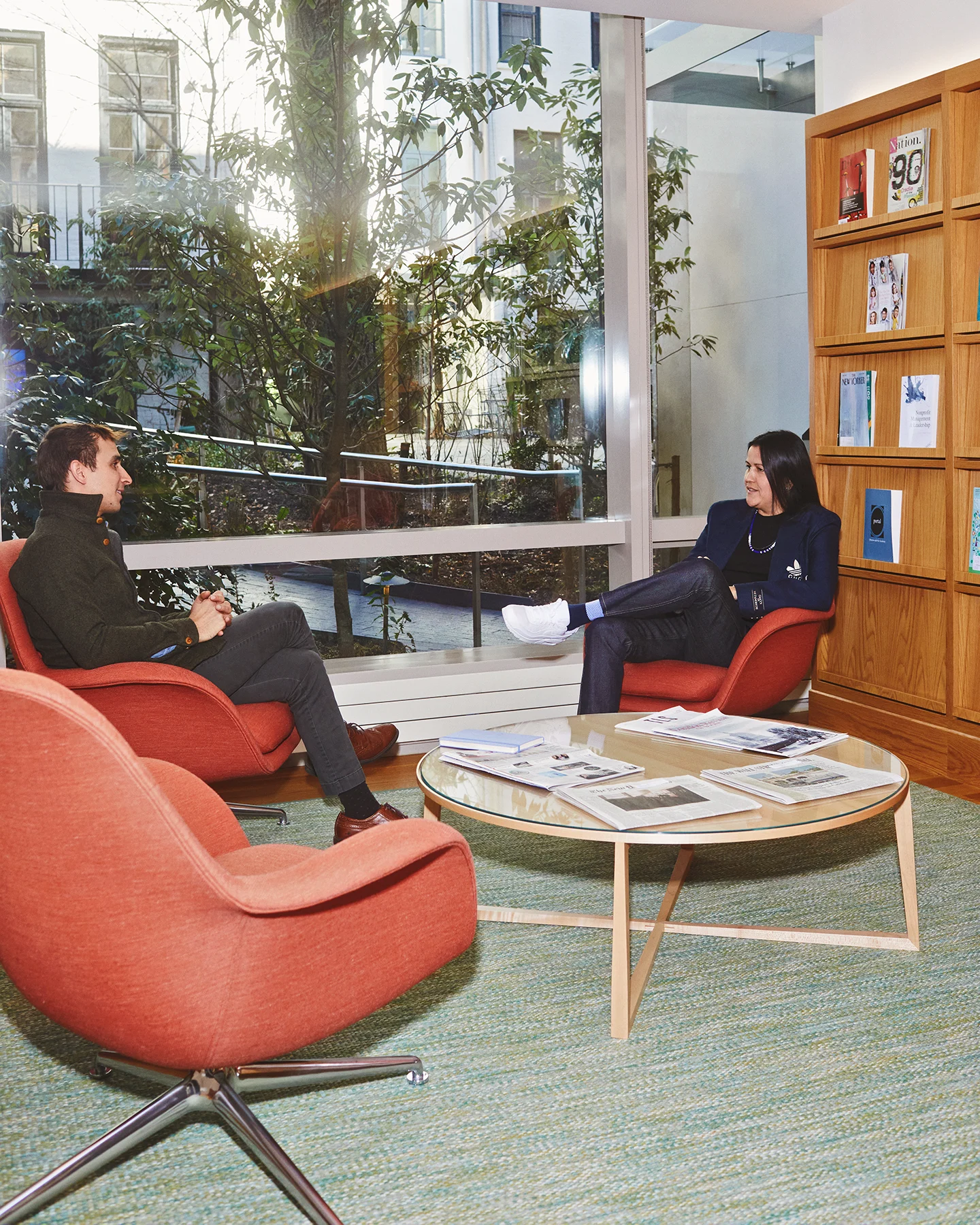 Two people, a man and an Indigenous scholar, sit across from each other in chairs and talk to one another. 