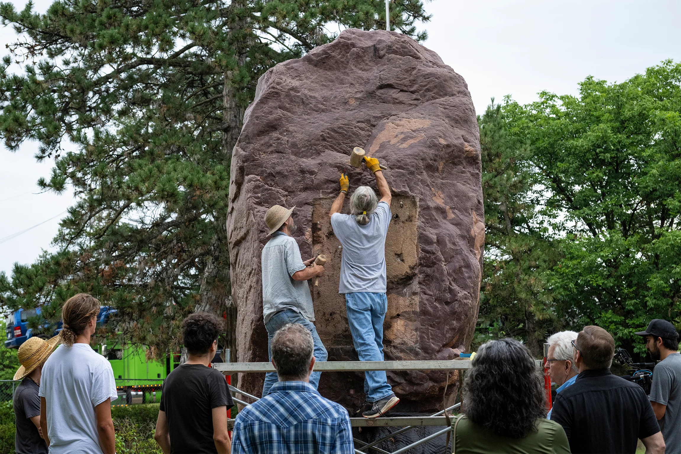 Two men work to remove a plaque from a large rock