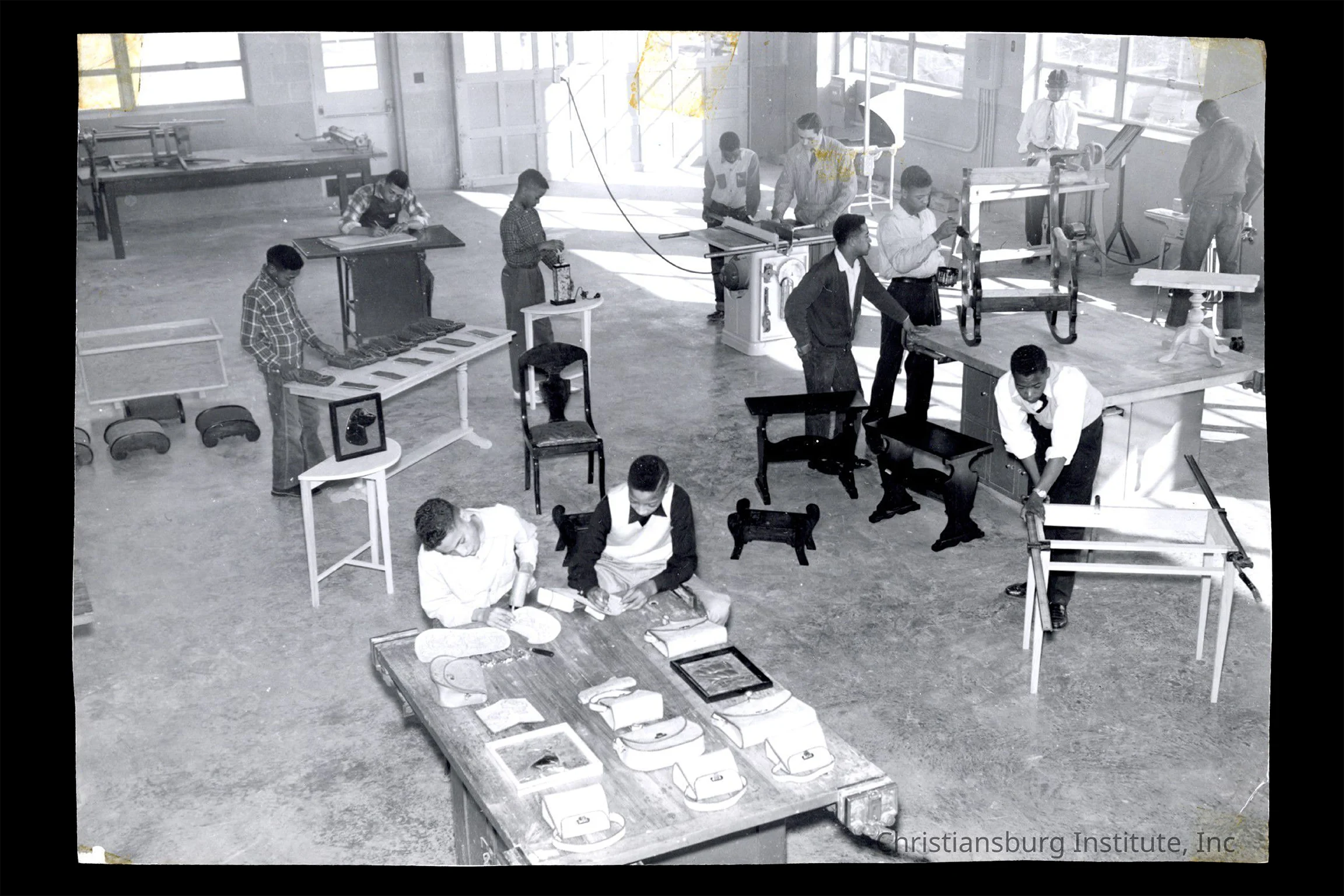 Black-and-white photograph of students working in a vocational woodworking and furniture-making classroom, using tools and assembling furniture in a large workshop space.