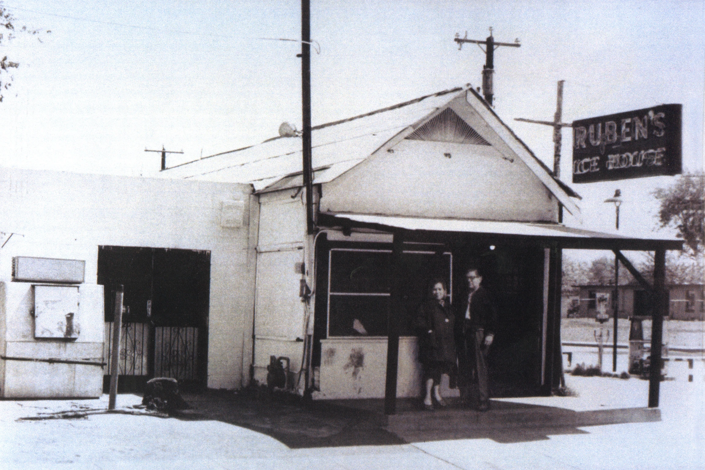 A couple stands in front of a small white building with an old neon sign that says "Ruben's"