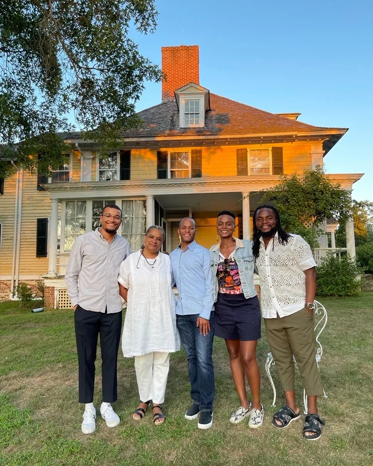 A group of five people stand outside in front of a historic manor. 