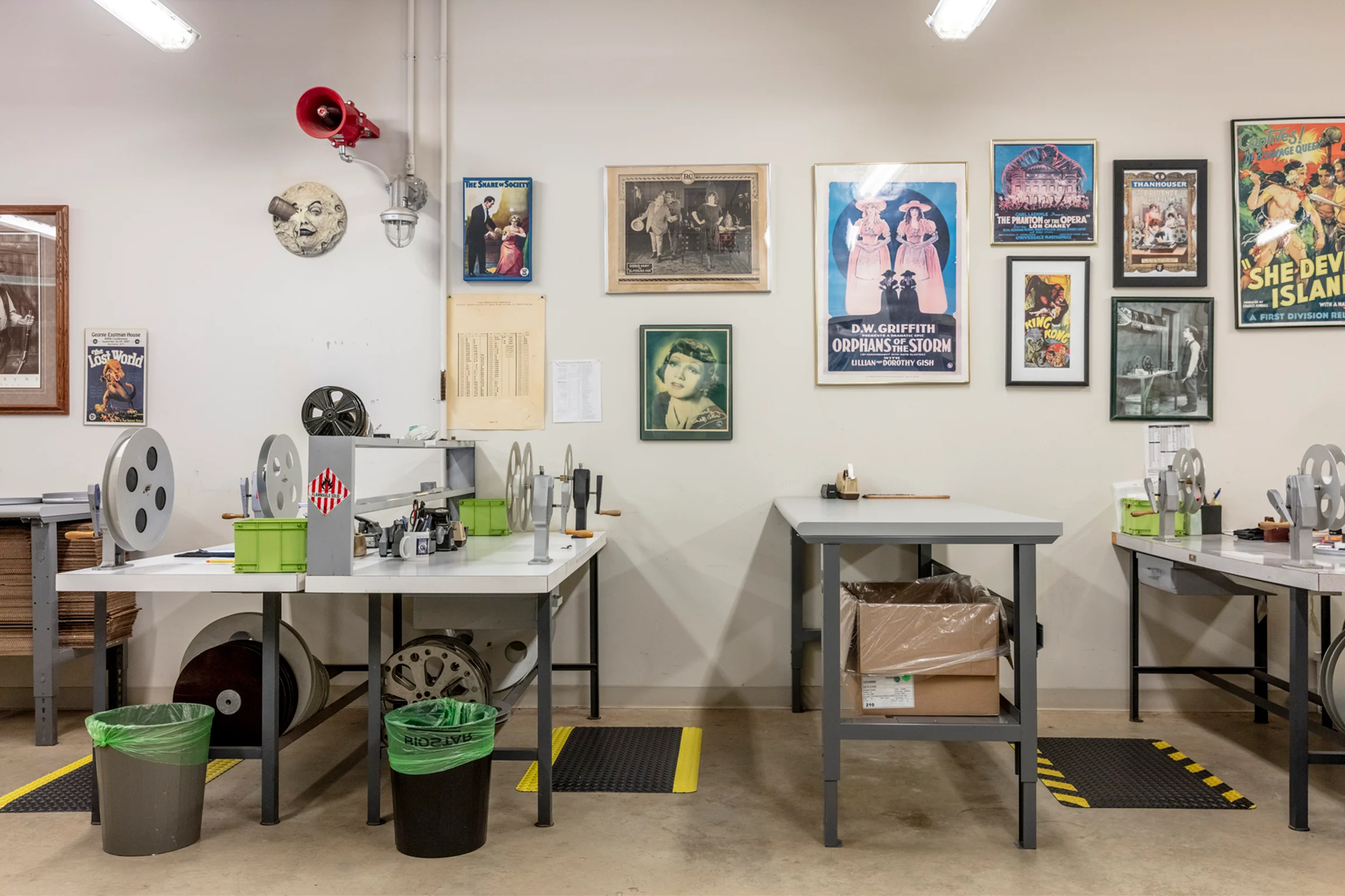 Desks along a white wall that has several framed vintage posters hung on it