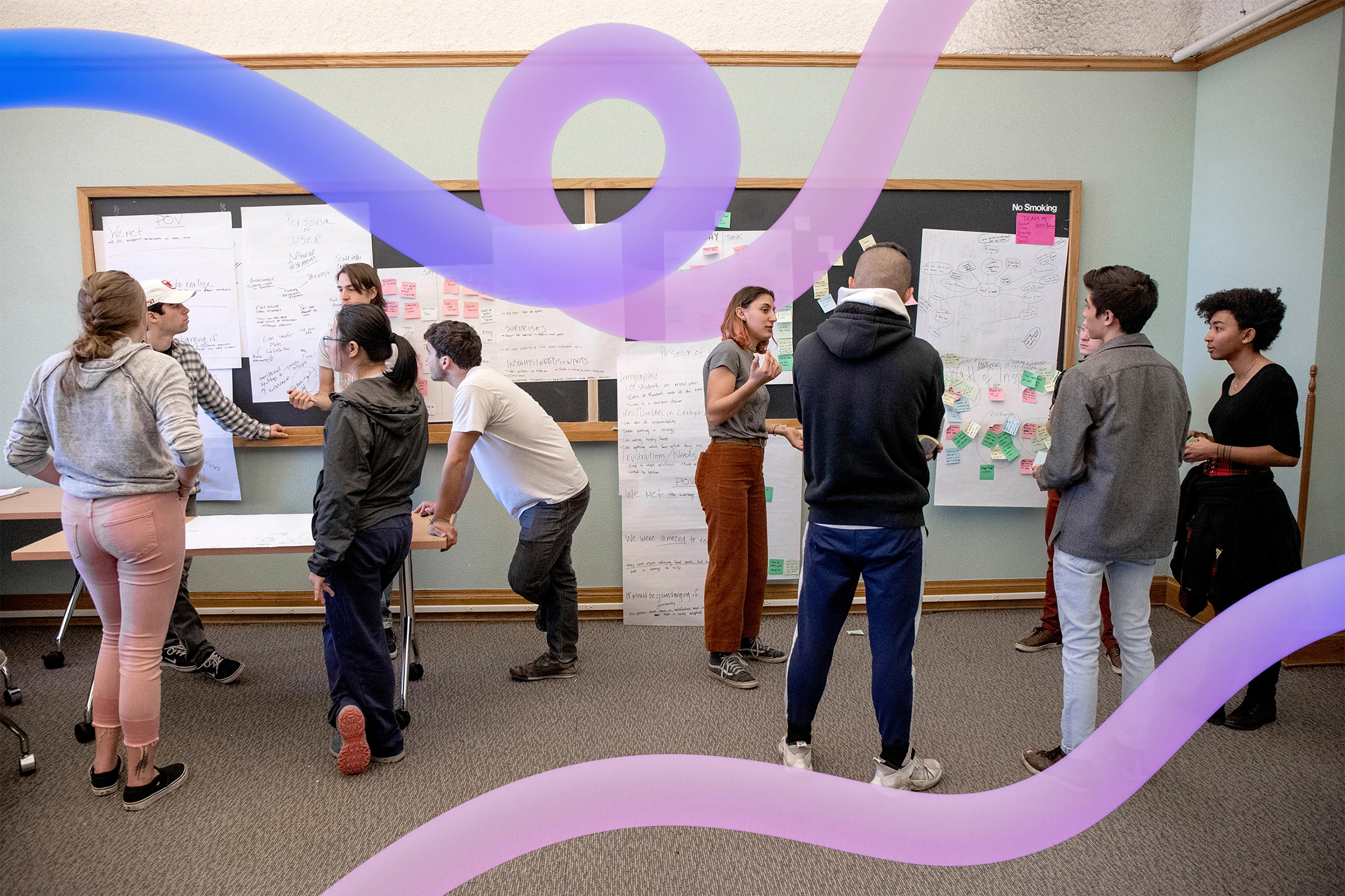 In a campus classroom, college students ideate in small groups with paper and notes hanging on the walls and chalkboards