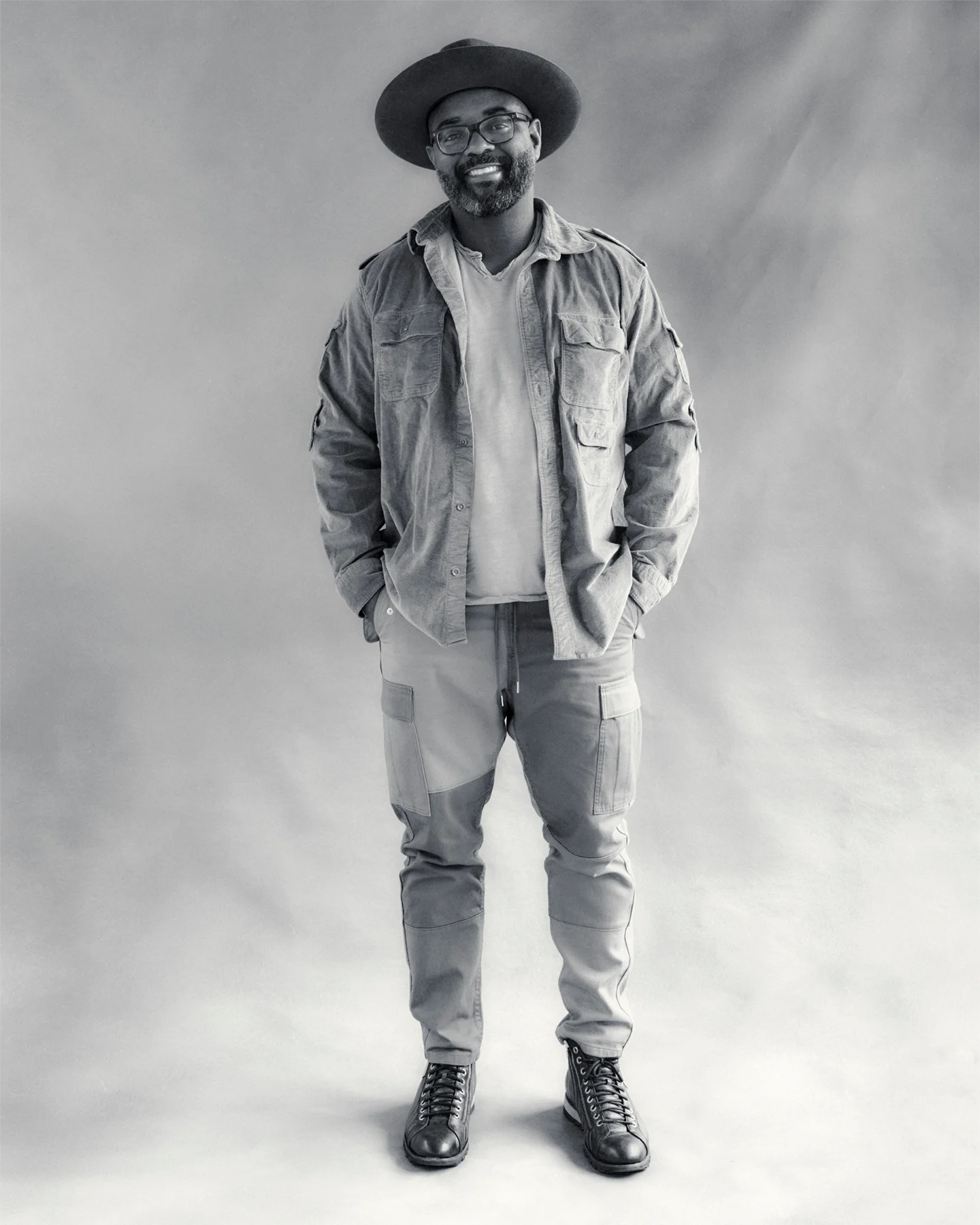In black and white, a portrait of a Black poet who is wearing a hat and looking at the photographer