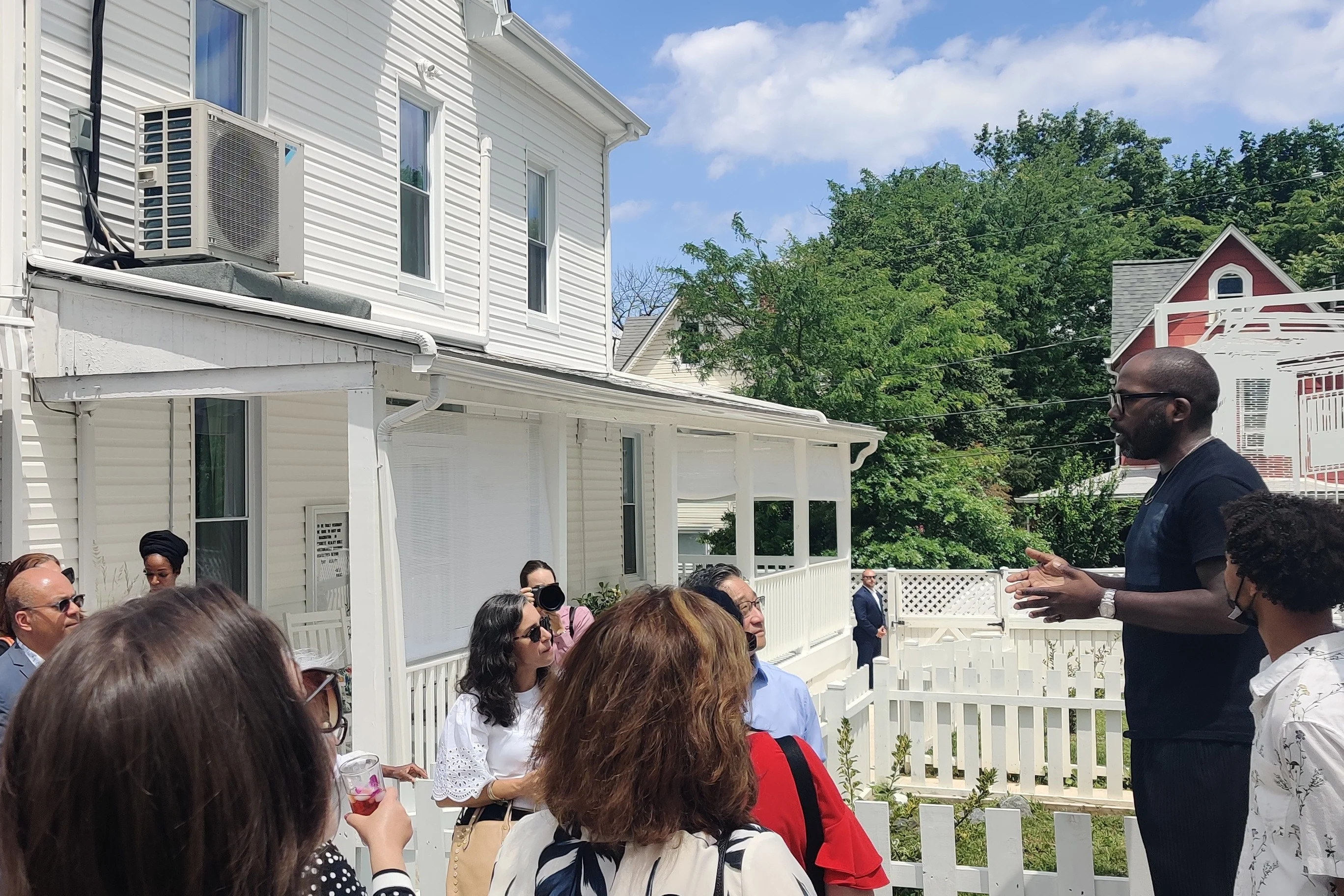 A Black artist stands outside a restored house and addresses a group of visitors.