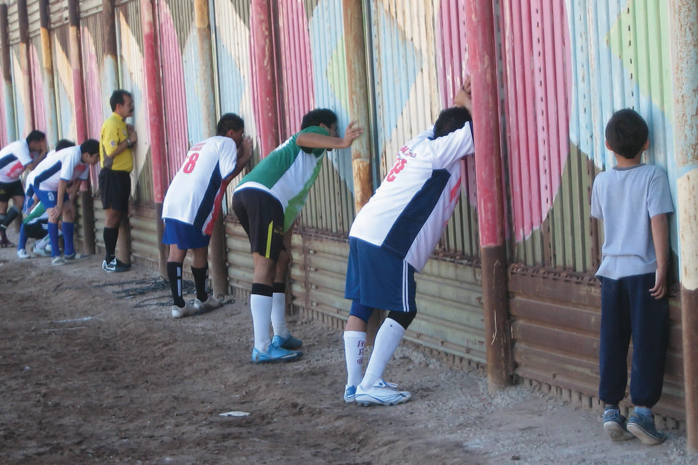 Seven people dressed in team jerseys and shorts stand facing a wall
