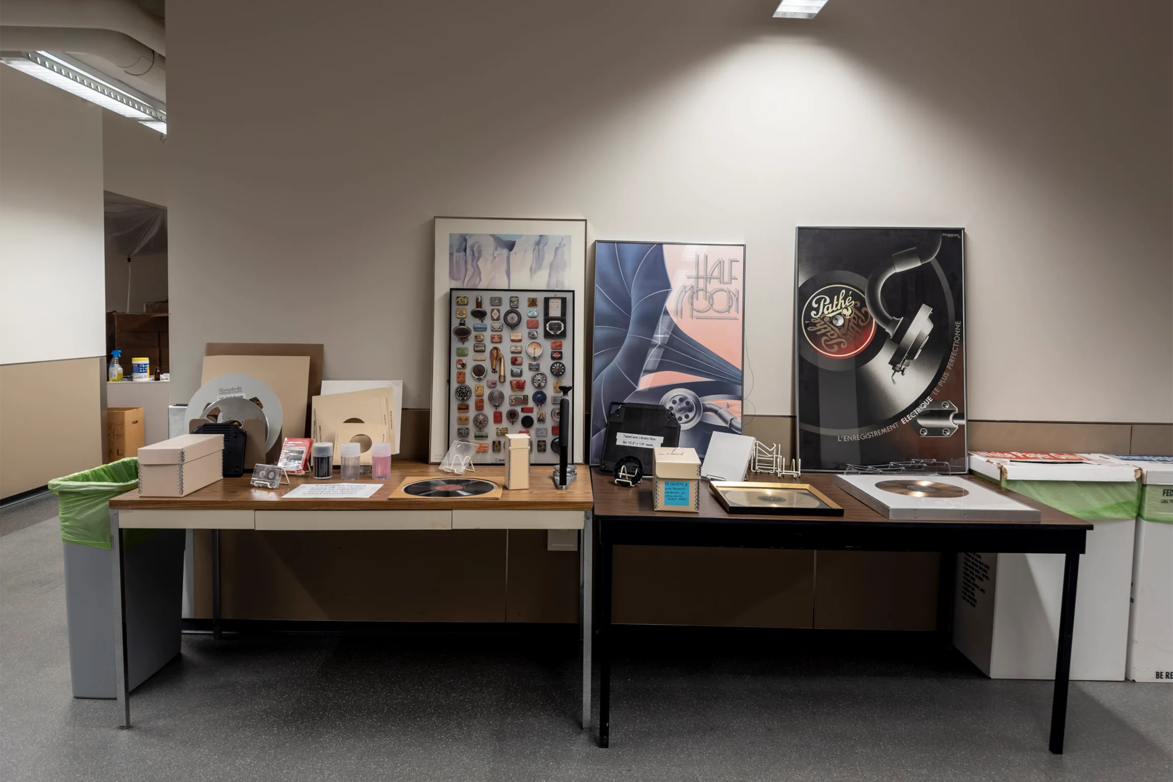 Two desks along a dimly lit wall containing various items including framed vintage posters and albums