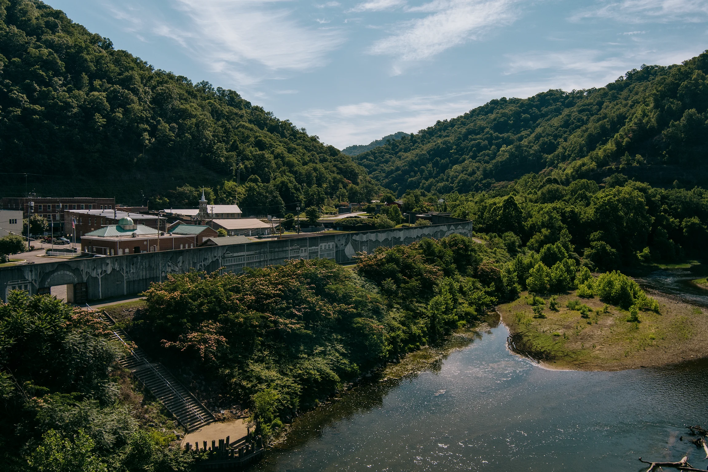 A river winds past a small town surrounded by forested mountains.