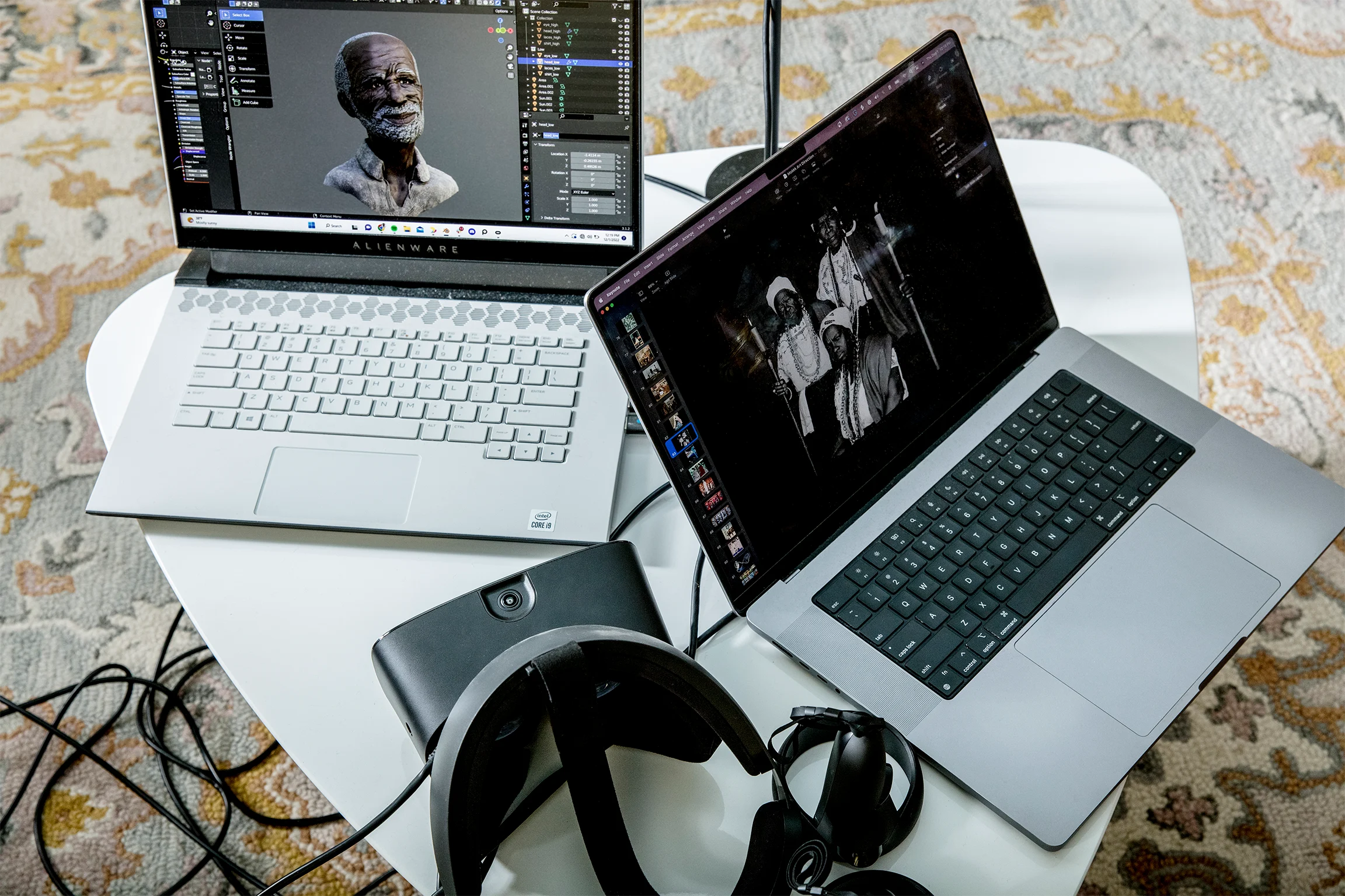 Two laptops sit on a white table next to a virtual reality headset