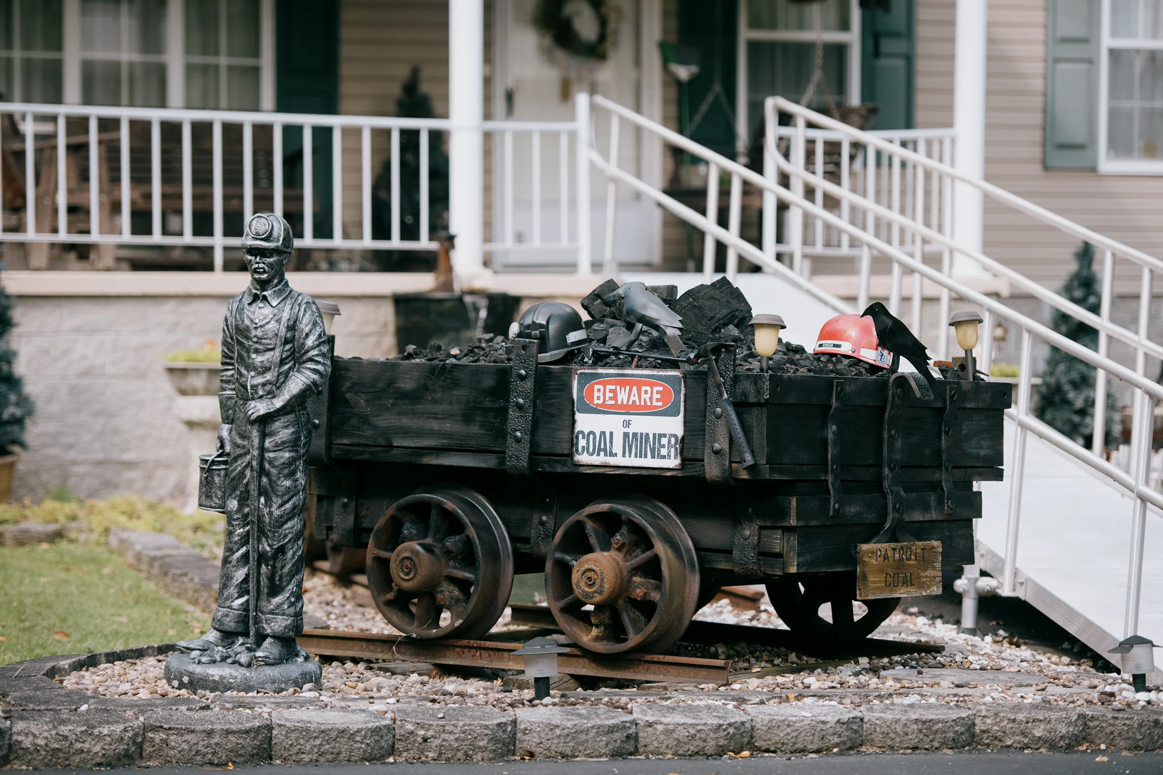 Coal mining memorial featuring a miner statue and a coal cart filled with mining equipment outside a home.