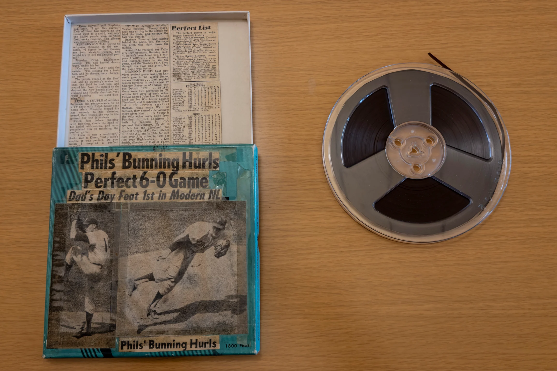 The top of a wooden desk with an old newspaper clipping on the left side and a film reel on the right