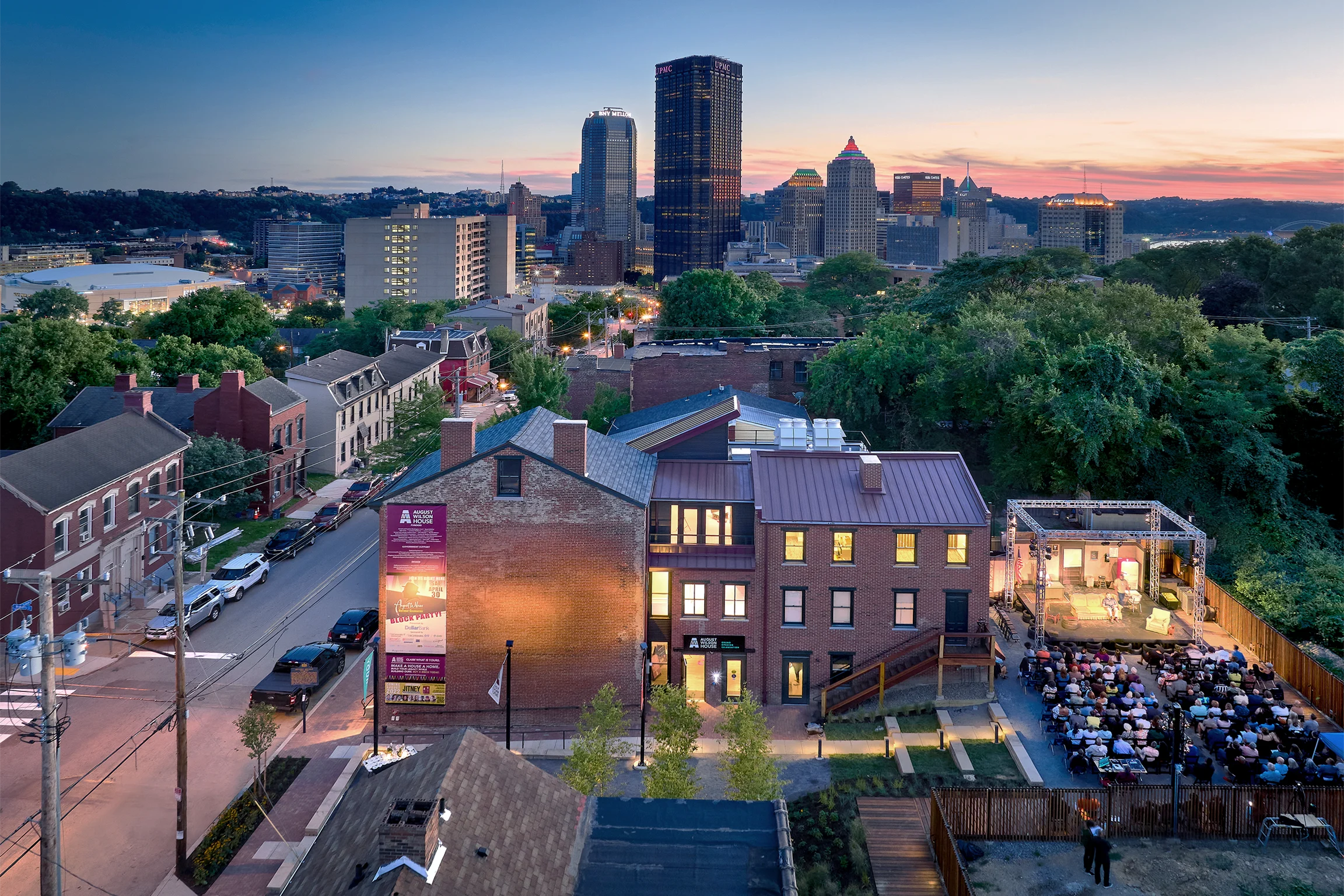 A view of downtown Pittsburgh at sunset with brick buildings lining a street in the foreground
