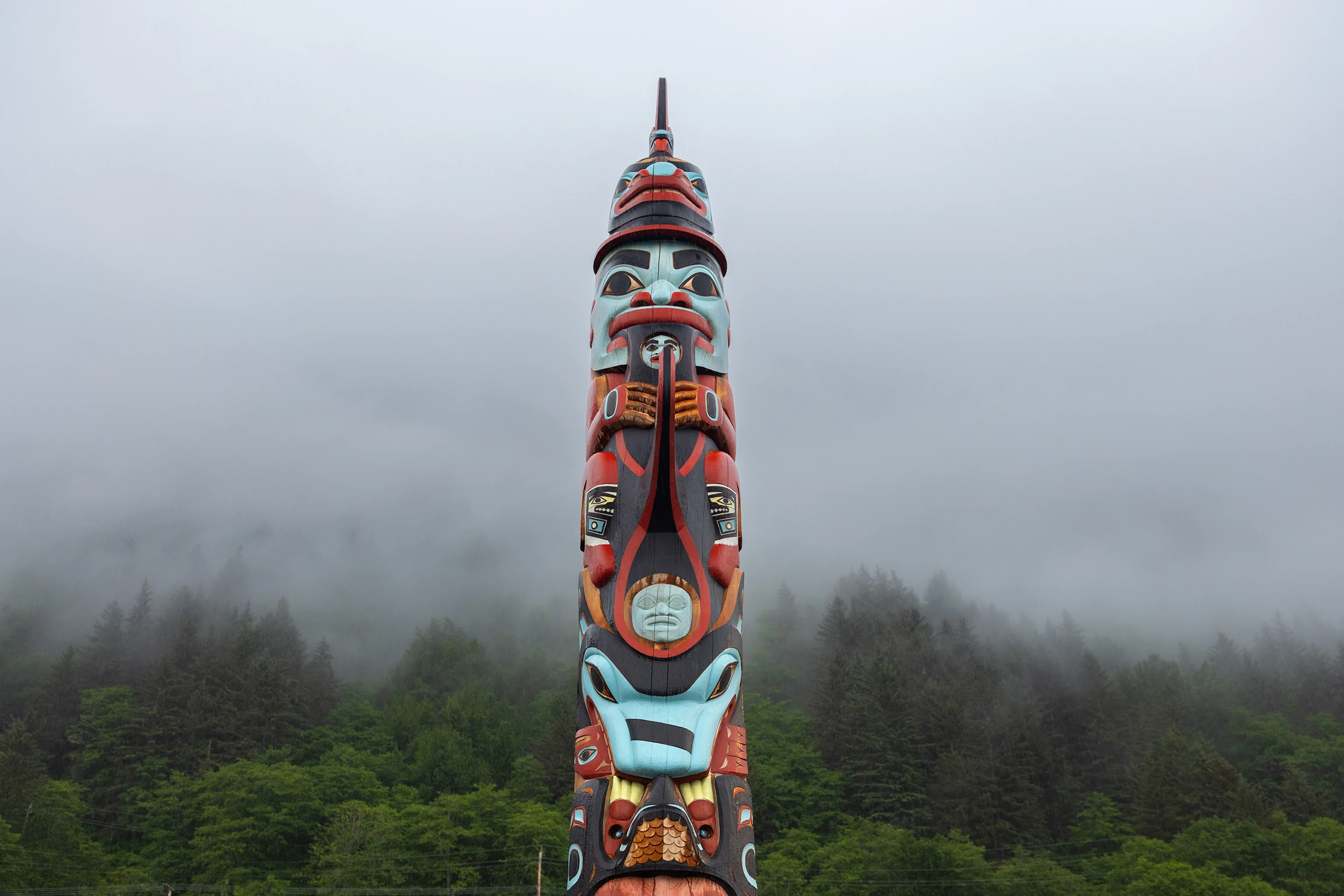 A multicolored painted totem pole set in front of a foggy forest landscape