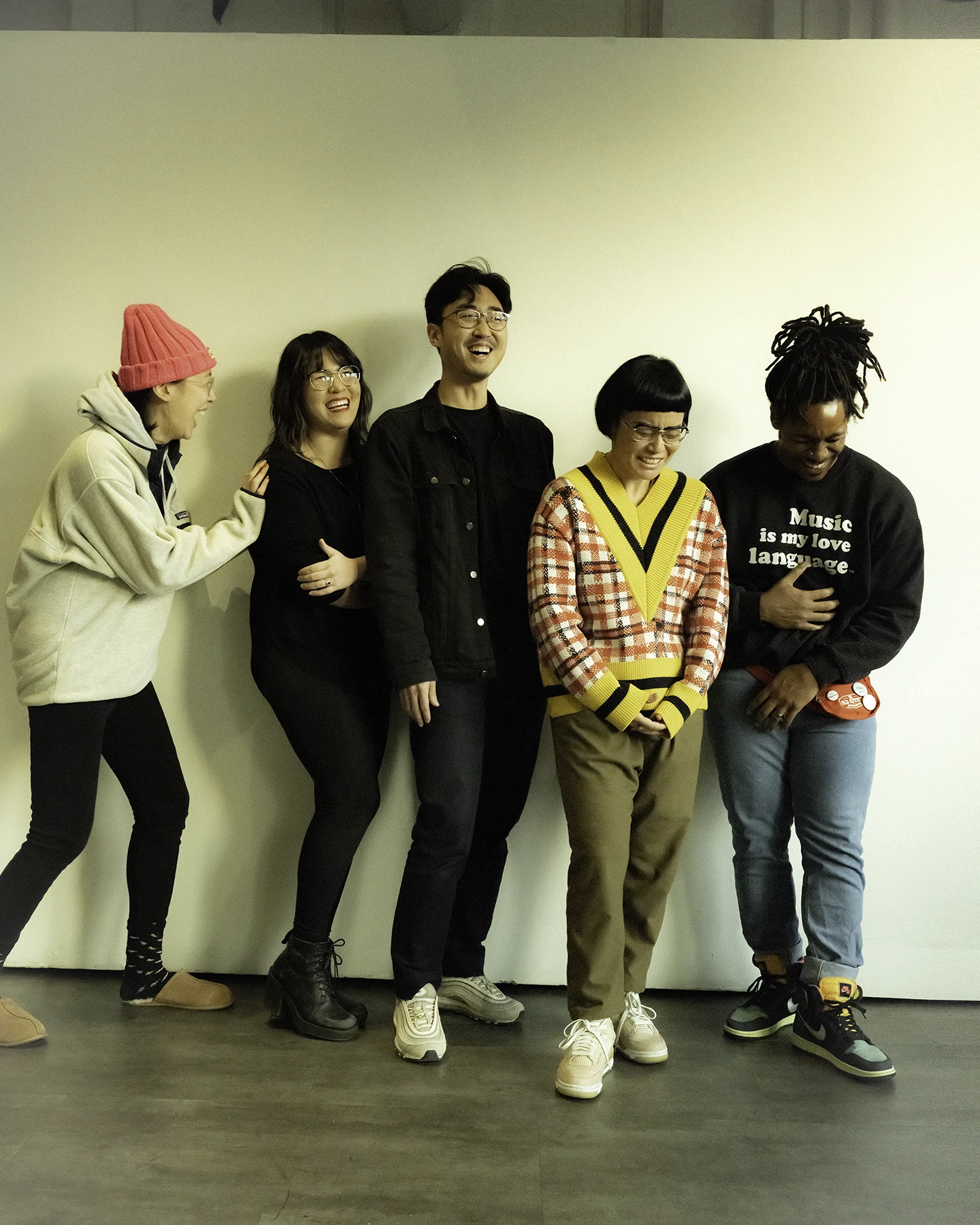 Five people stand together in a group photo. They are laughing and smiling.