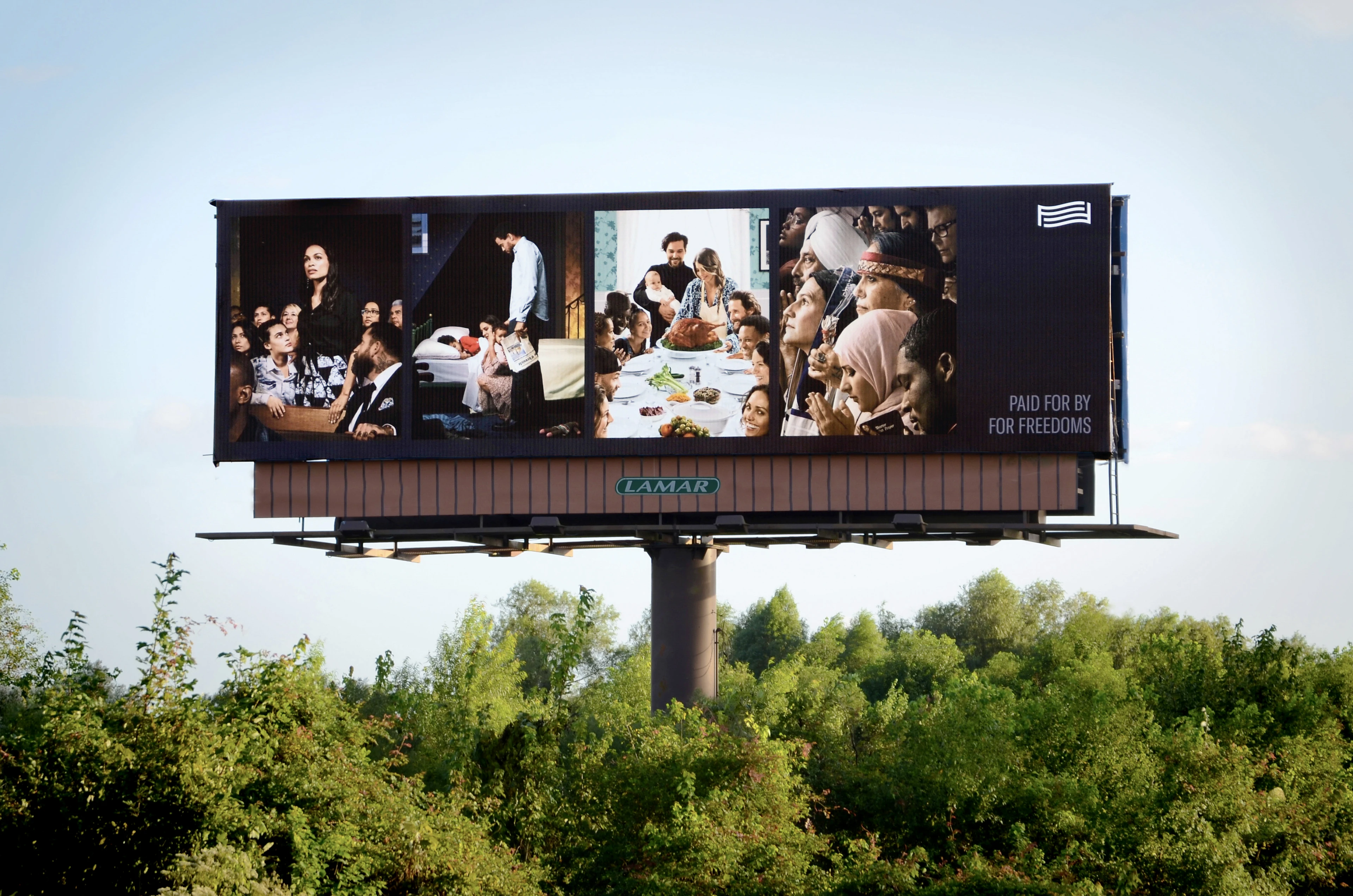 A highway billboard stands above a tree line and depicts four artist-created images that reference a set of historical illustrations