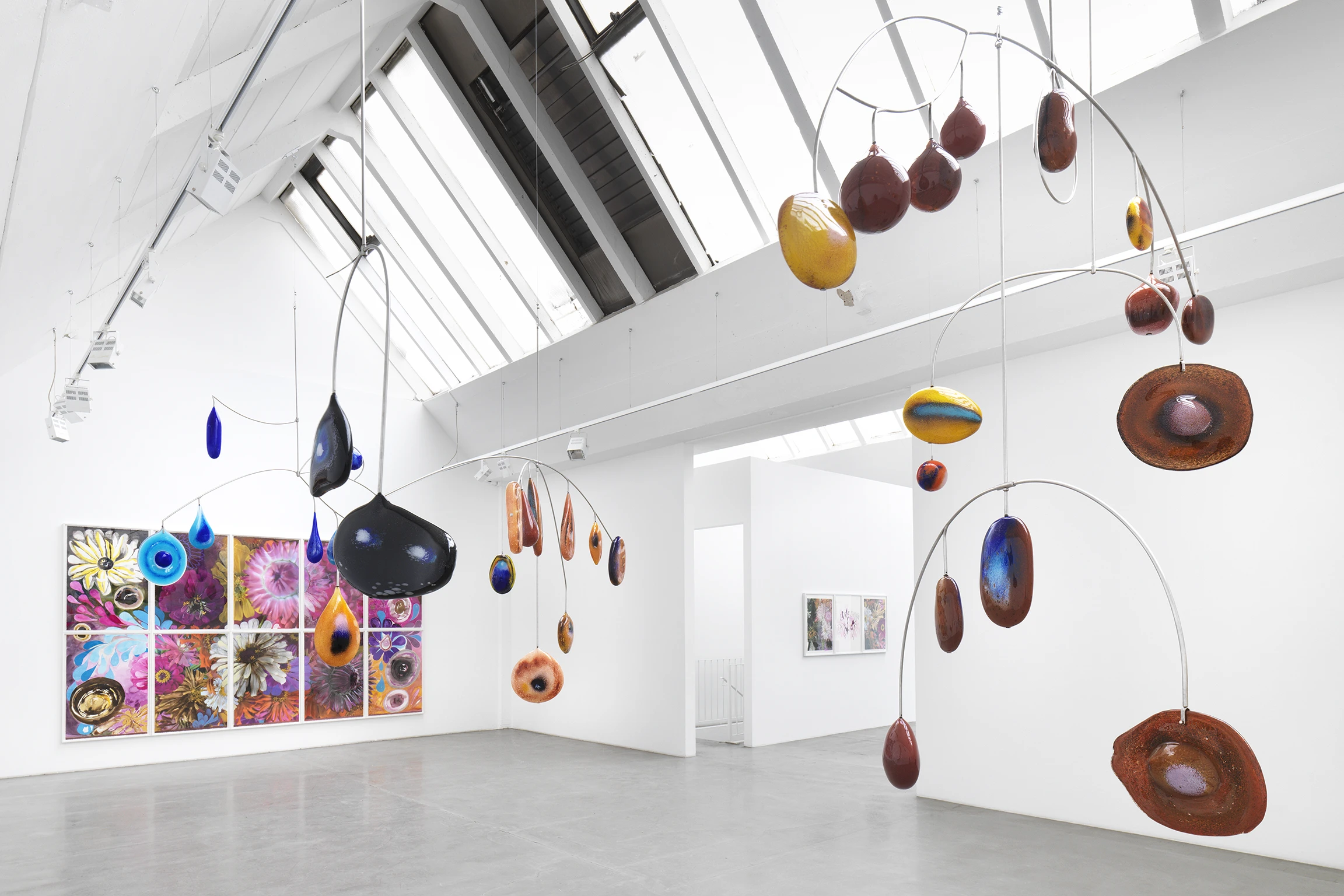 In a white-walled gallery space a colorful mobile hangs from the ceiling