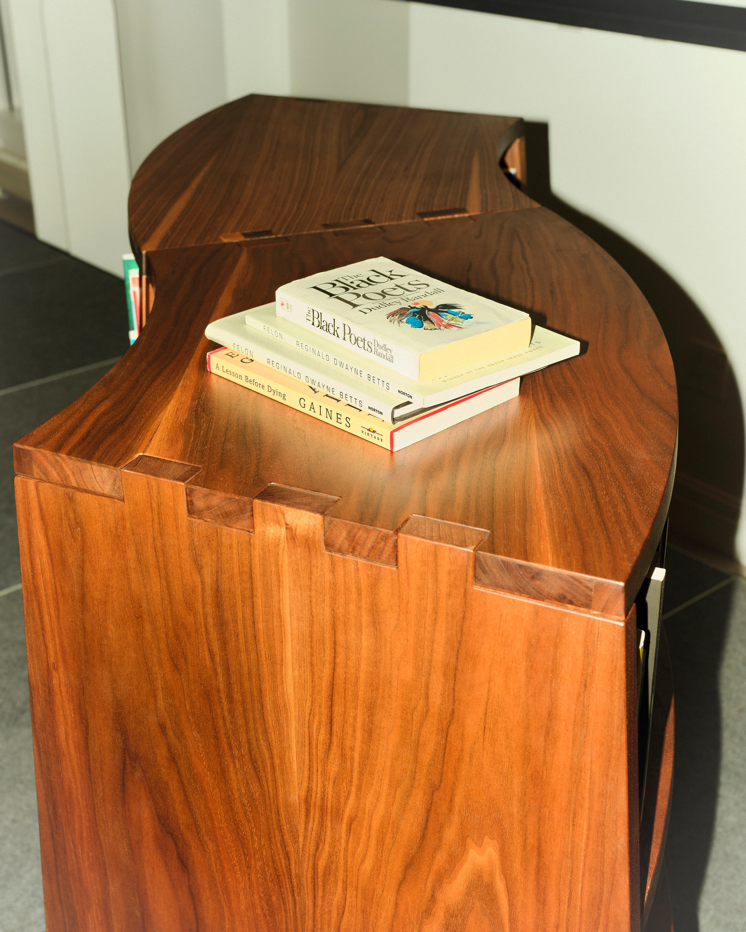 Wooden table with smooth, curved edges holds a stack of books, including "The Black Poets."