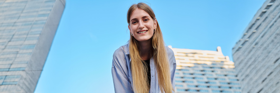 Una mujer sonriente con cabello largo y liso fotografiada al aire libre contra un cielo azul.