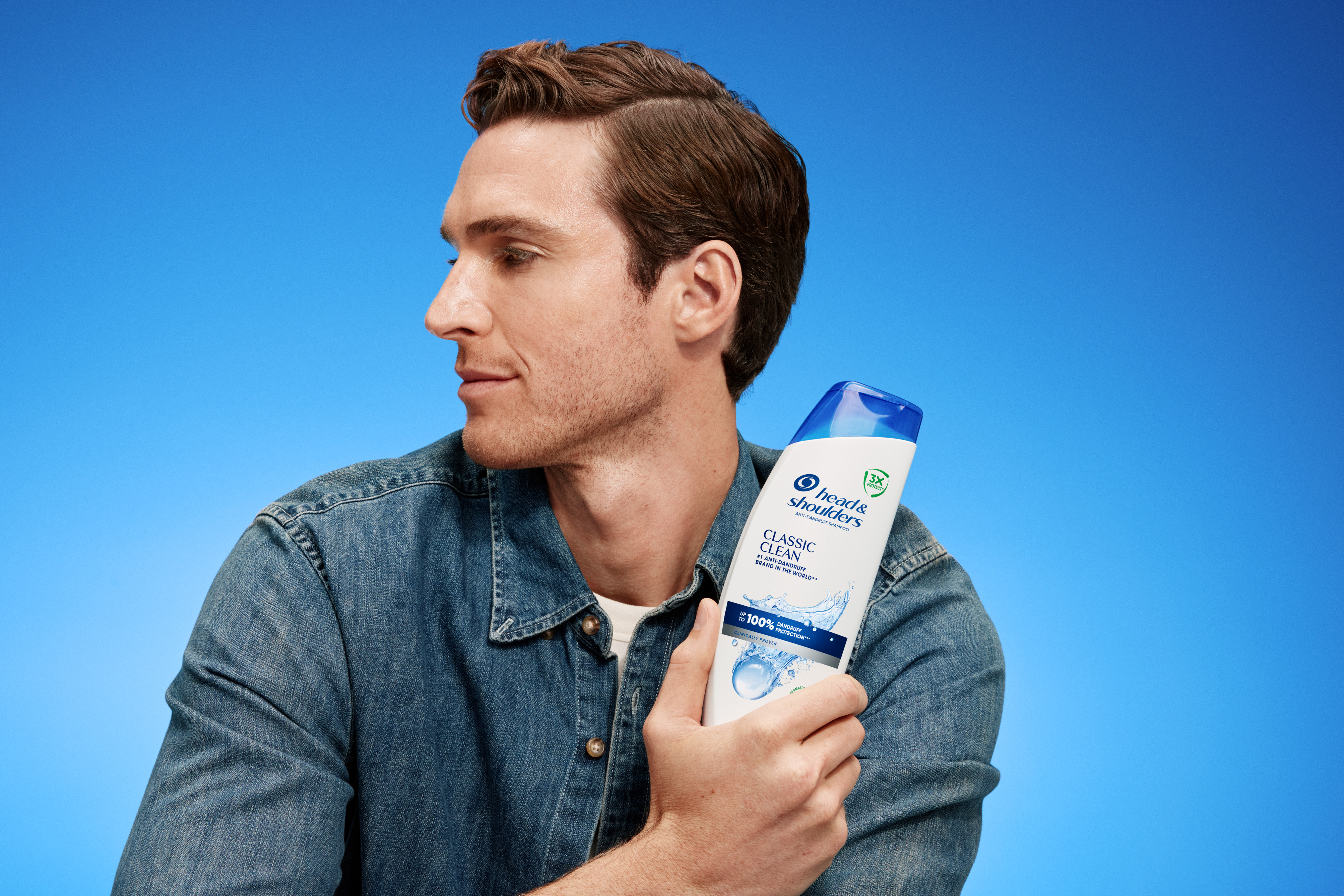 Hombre muestra el champú Classic Clean sobre fondo azul