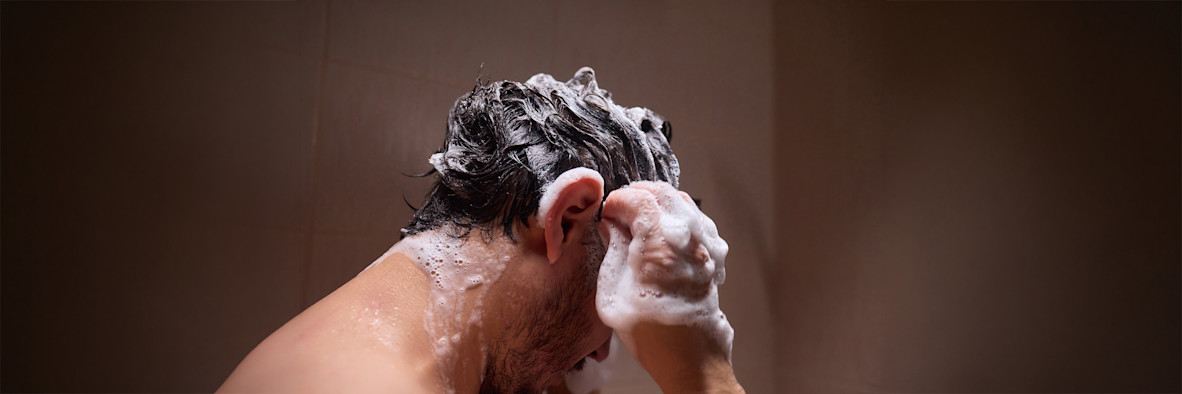Unas manos aplican una rica espuma de champú a través del cabello oscuro y mojado durante el lavado.