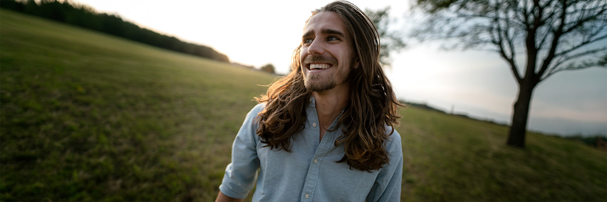 Un hombre con cabello largo y natural está de pie en un paisaje al aire libre con el viento en su cabello.