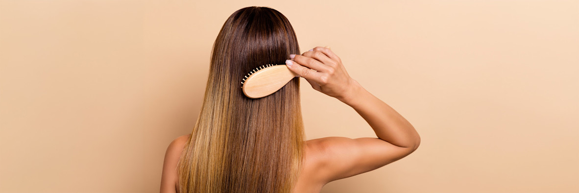 Una mujer vista desde atrás se cepilla suavemente su cabello largo, liso y castaño.