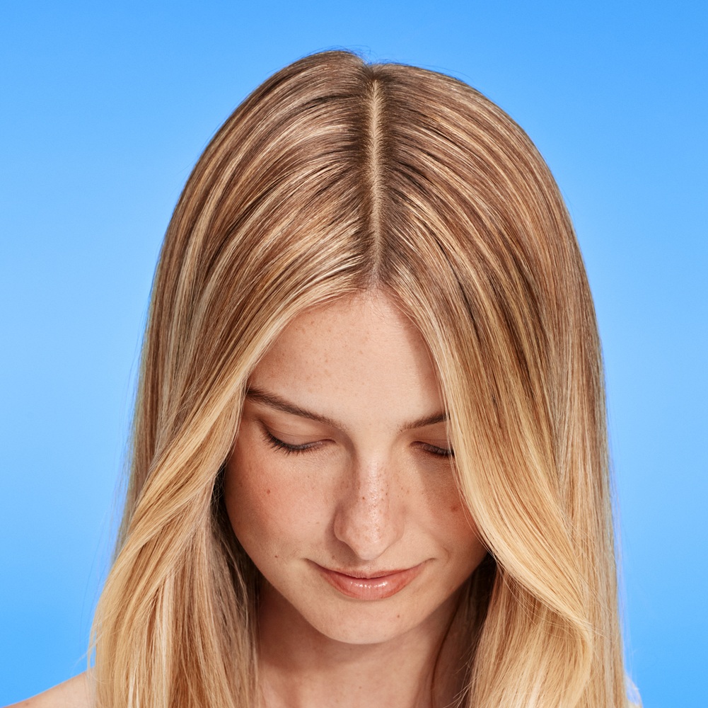 Mujer rubia con la cabeza inclinada muestra un cuero cabelludo sano y la raya
