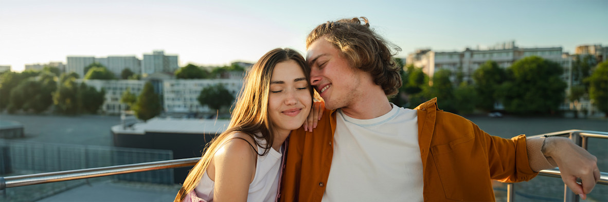 Una pareja se abraza afectuosamente en una azotea al atardecer, ambos con el cabello bien peinado.