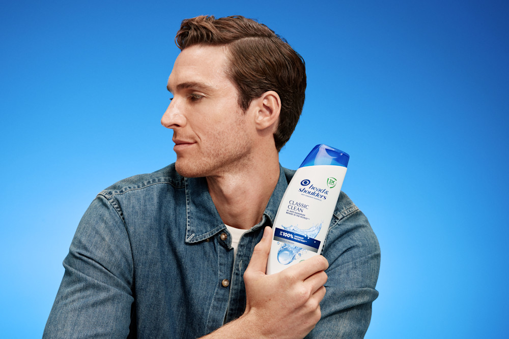 Hombre muestra el champú Classic Clean sobre fondo azul