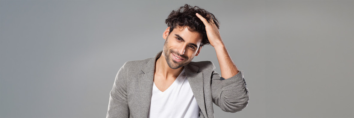 Un hombre con una camiseta gris se lleva la mano a la cabeza con expresión de frustración.