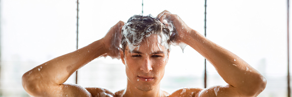 Un hombre se lava el cabello en la ducha con una espuma densa y burbujas cubriendo su cabeza.