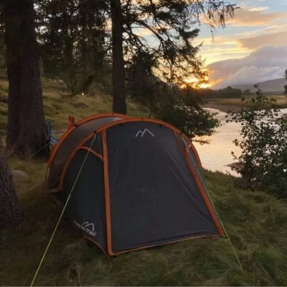 Tent pitched on river bank in front of tree