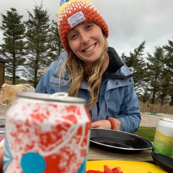 Woman smiling whilst sitting at a table with a plate and can of beer