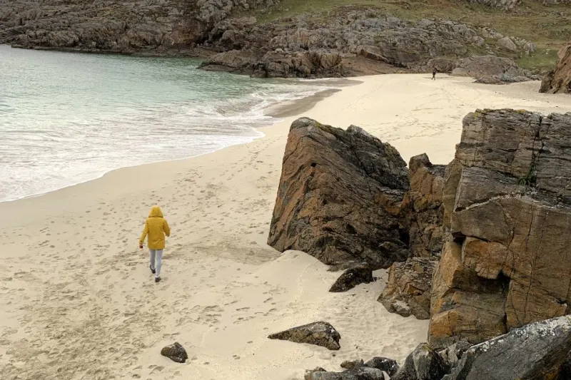 Woman wearing yellow coat walking across white sand beach