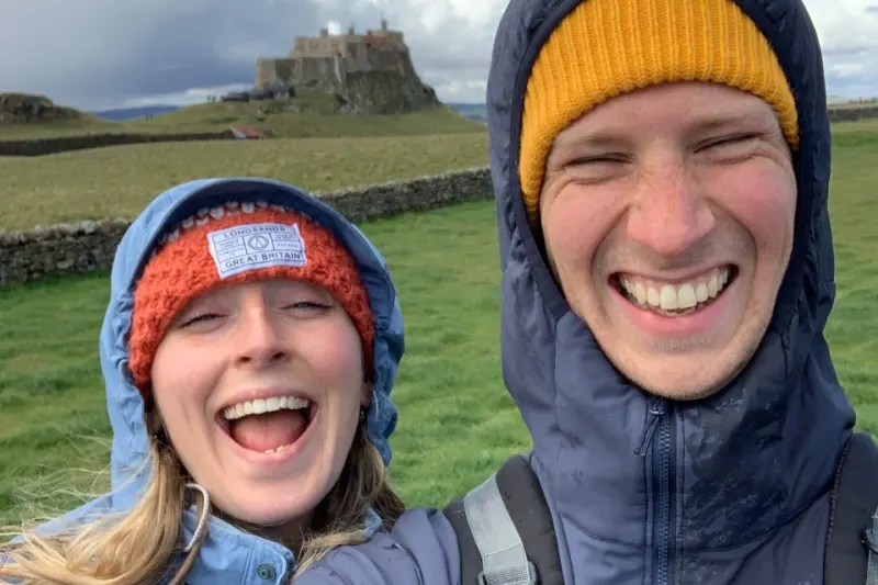 Woman and man smiling, wearing hats in front of castle