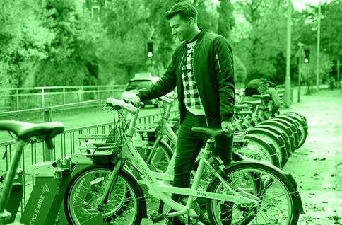 A man stood at a cycle hire station hiring a bike.