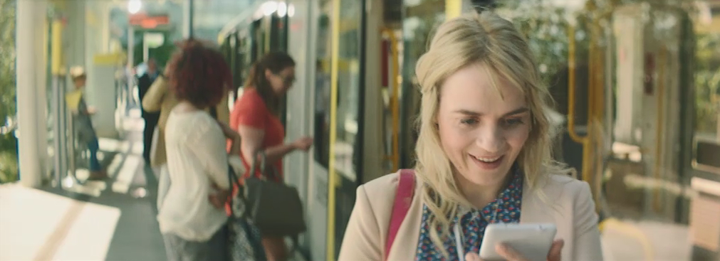 Picture from a Moonpig advert filmed on a tram stop, with a woman looking at her phone smiling