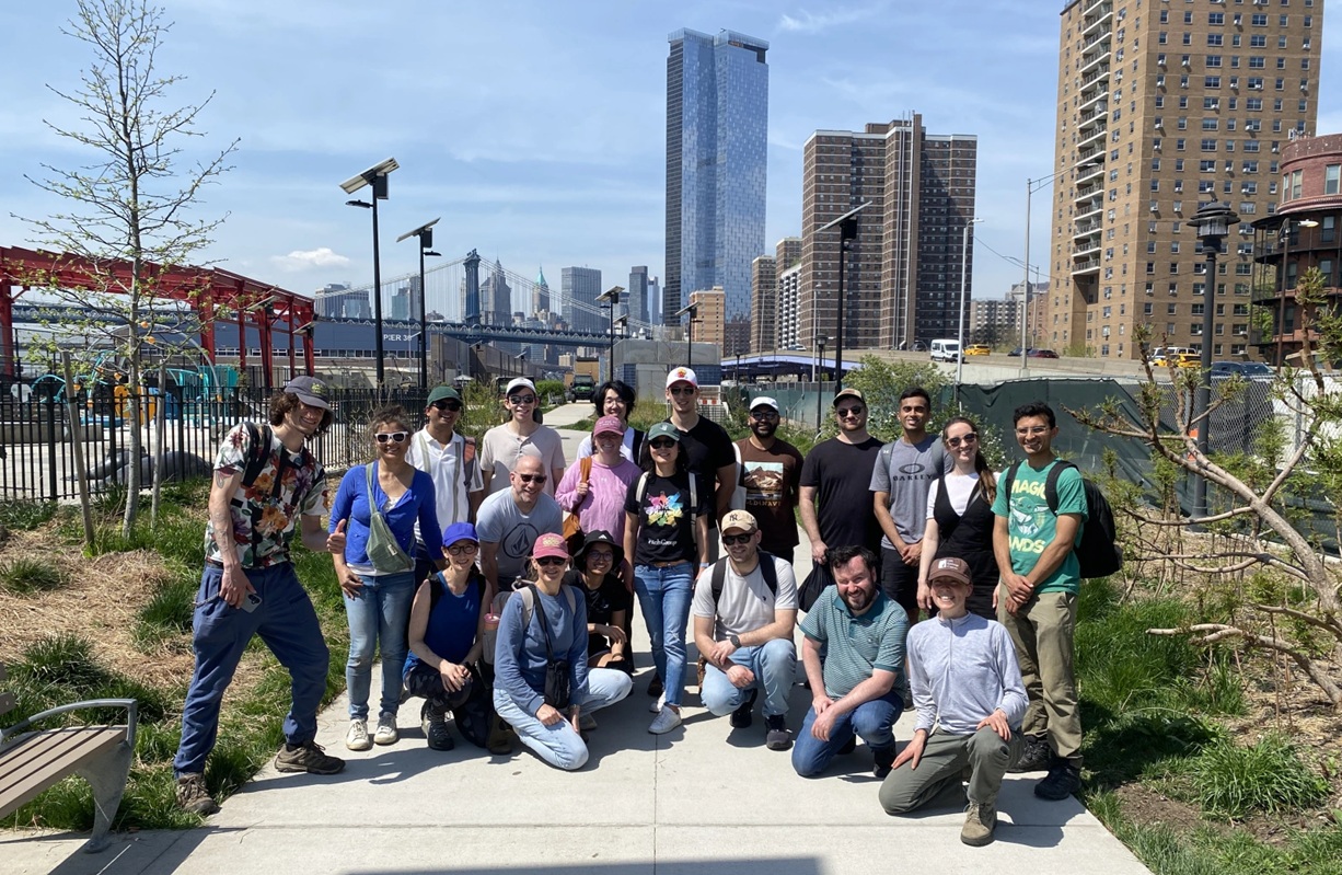 Group of people posing on a city walkway with skyscrapers and a bridge in the background on a sunny day. on Greenwave
