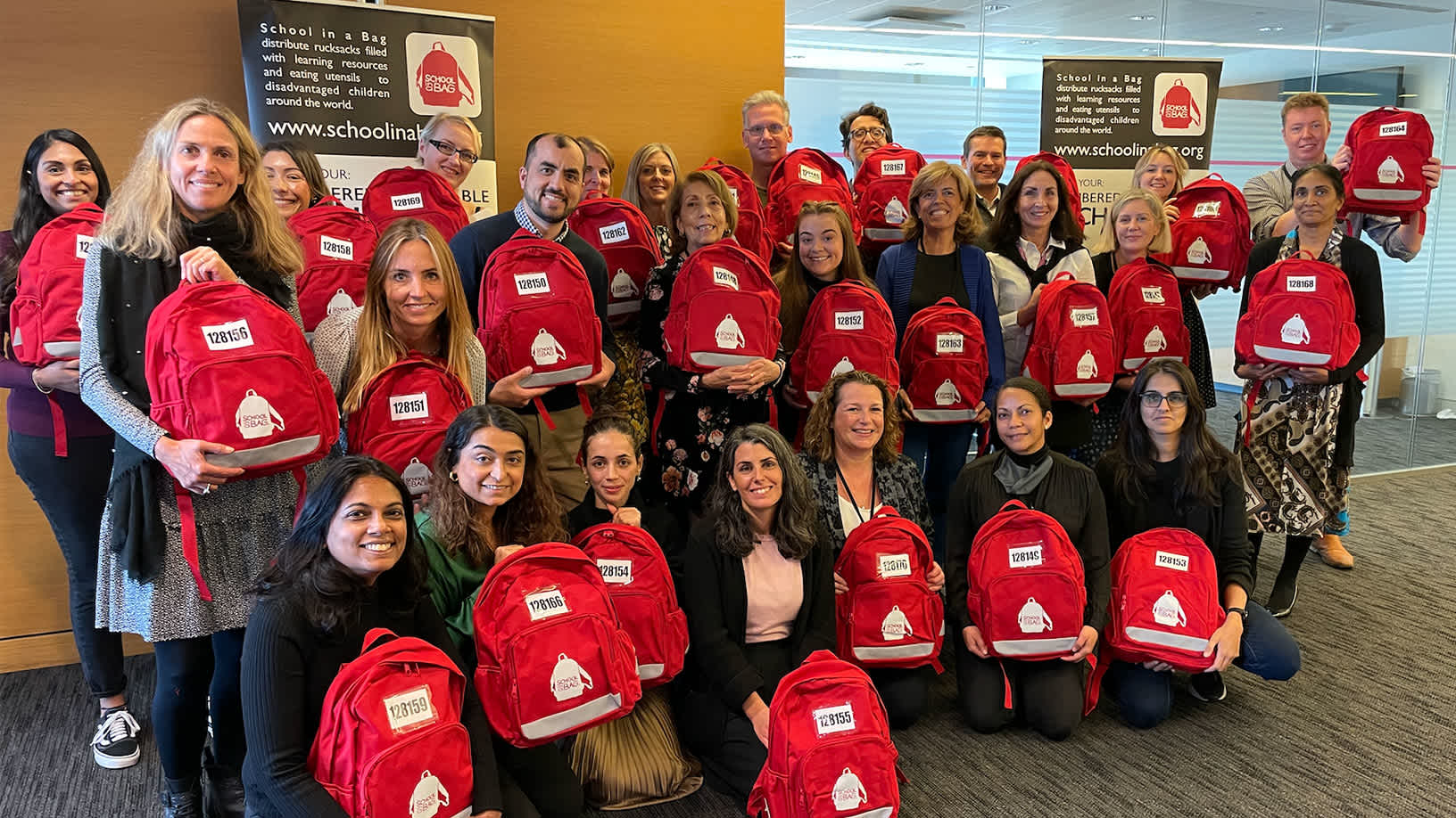 A large Fitch group employees holding red school bags on School Bags To Support Access To Education