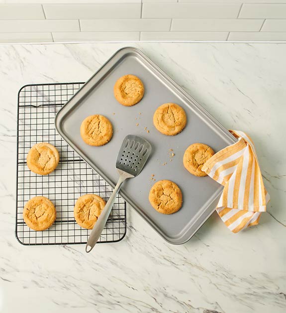 Cookie sheet with cookies on it with a striped yellow/white kitchen towel to the side