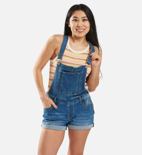 Woman model wearing a pair of medium blue wash shortalls with a orange, pink, white striped tank top.